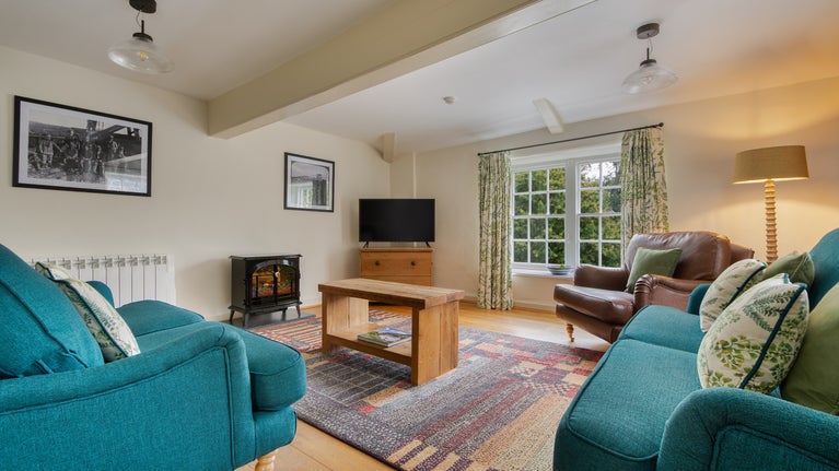 The seating area in the open-plan living space with a television, two sofas, an armchair and an electric fire at Penrose Stables, Cornwall